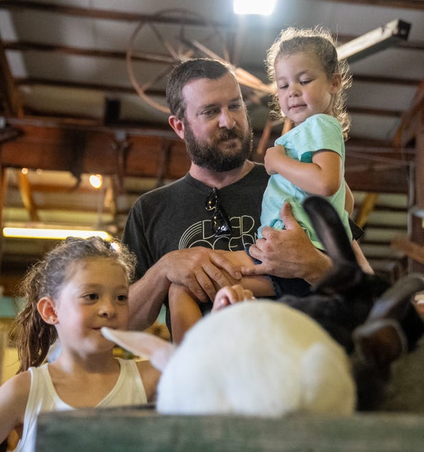 Addy McGovern, 7, Chris McGovern and June McGovern, 4, pet the Beveren bunnies at Pioneer Village on Friday, July 28, 2023, at the Indiana State Fair in Indianapolis.